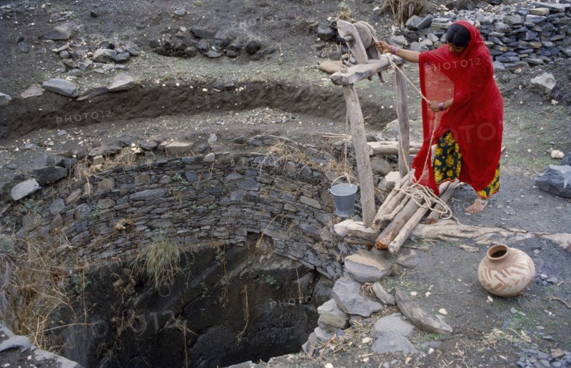 INDIA, Rajasthan, Banswada, Woman collecting water from open well.