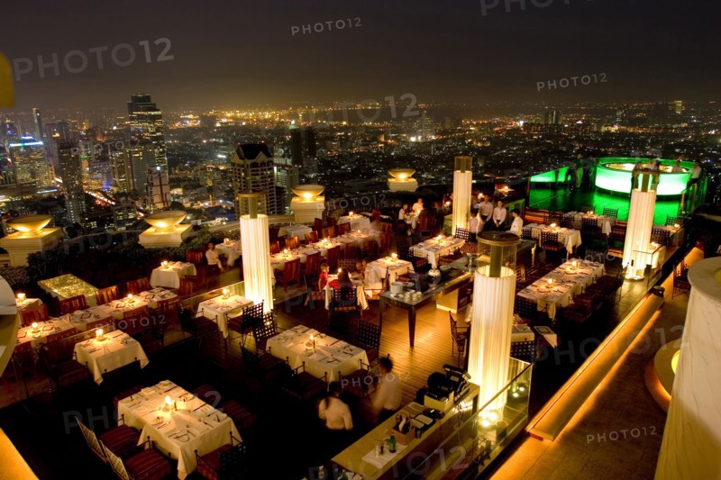 THAILAND, Bangkok, Sorocco Restaurant. View over people dining at tables lit up with light displays and the Bangkok Skyline in the background.