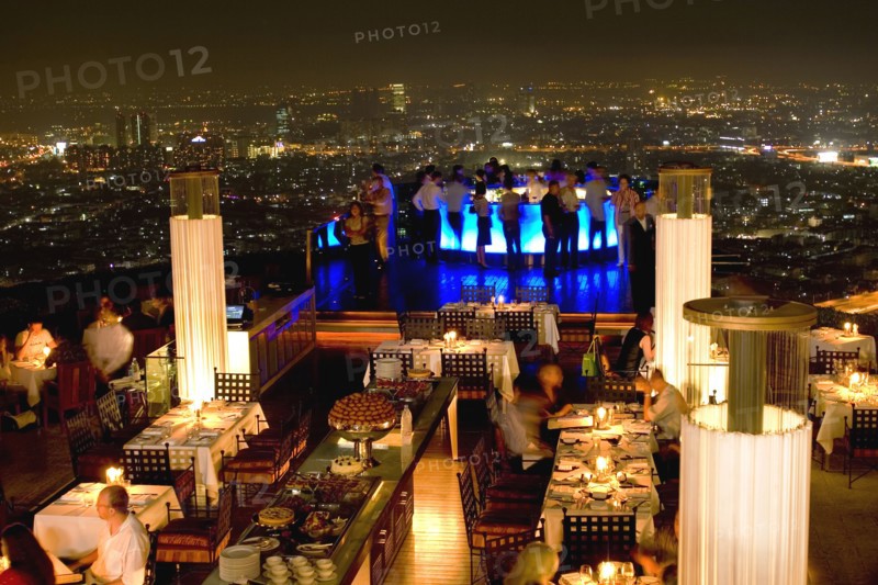 THAILAND, Bangkok, Sorocco Restaurant. View over people dining at tables lit up with light displays and the Bangkok Skyline in the background.