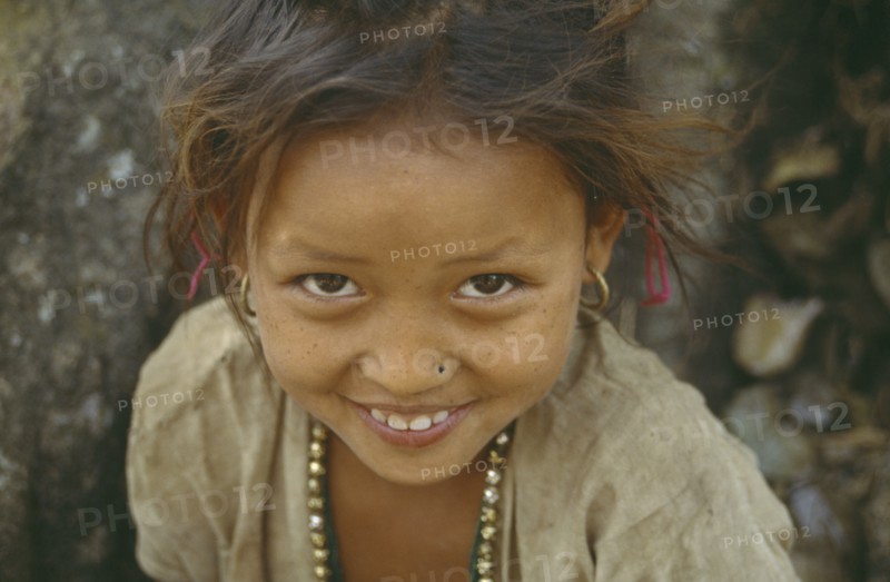 NEPAL, Dhankuta, Head and shoulders portrait of smiling young girl looking up to camera.