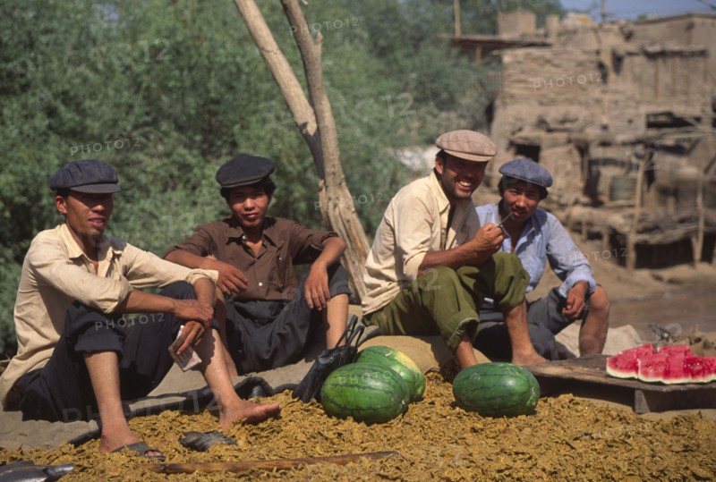 CHINA, Xinjiang Province, Kashgar, Group of Tajik men sat on ground eating water melon