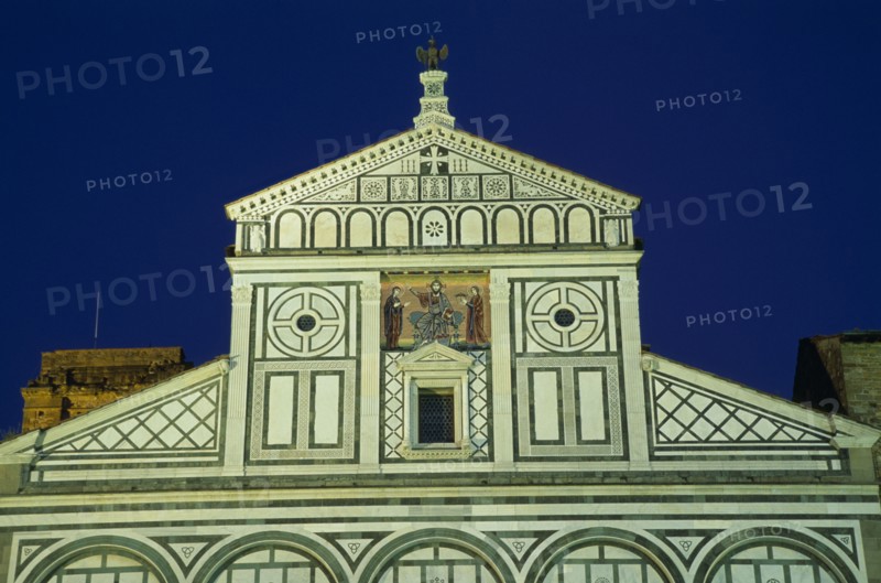 ITALY, Tuscany, Florence, San Miniato al Monte Romanesque church begun in 1018.   Exterior facade with geometric marble patterning and steps to entrance illuminated at night.
