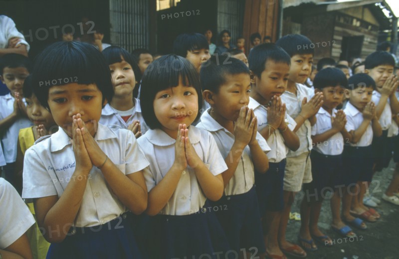 THAILAND, Tap Gaen, Line of school children giving traditional Thai greeting or wai with palms together and fingers extended.