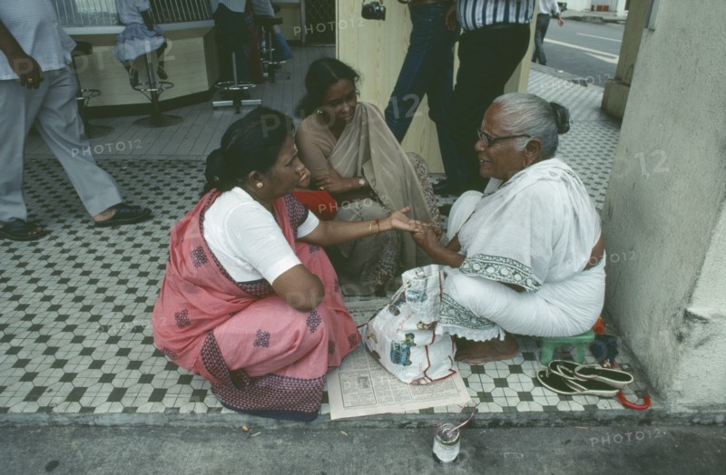 SINGAPORE, Little India, Sidewalk palm reader with women customers on Seragoon Street.