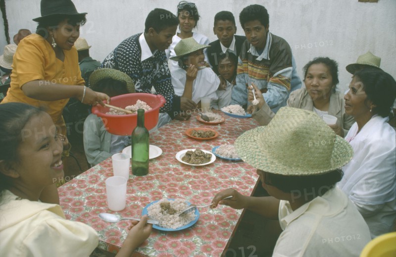 MADAGASCAR, Antananarivo, Large group of people having a meal of meat and rice.  Rice is a staple food and eaten at all meal times.