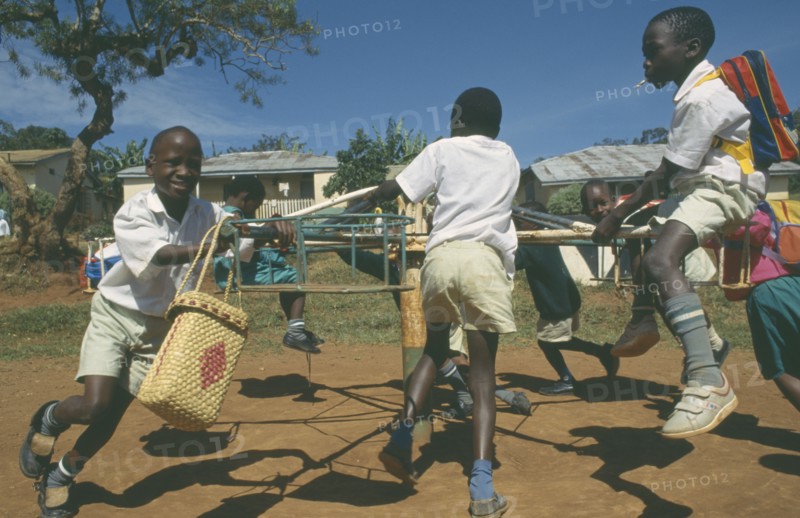 UGANDA, Mengo, Primary school children playing on roundabout. Young boy smoking cigarette.