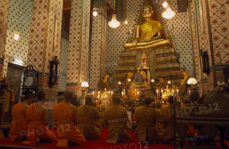 THAILAND, Bangkok, "Monks pray, kneeling down in front of large golden Buddha at Wat Arun. The Temple of Dawn."