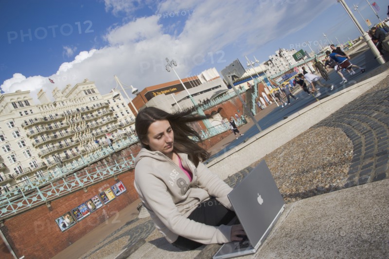 ENGLAND, East Sussex, Brighton, Woman using a laptop to surf the internet  in the free WiFi zone on the beach between the piers