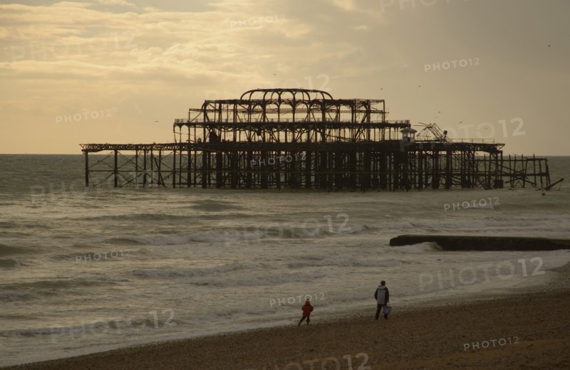ENGLAND, East Sussex, Brighton, The ruined West Pier with a man and small child walking together along shoreline.