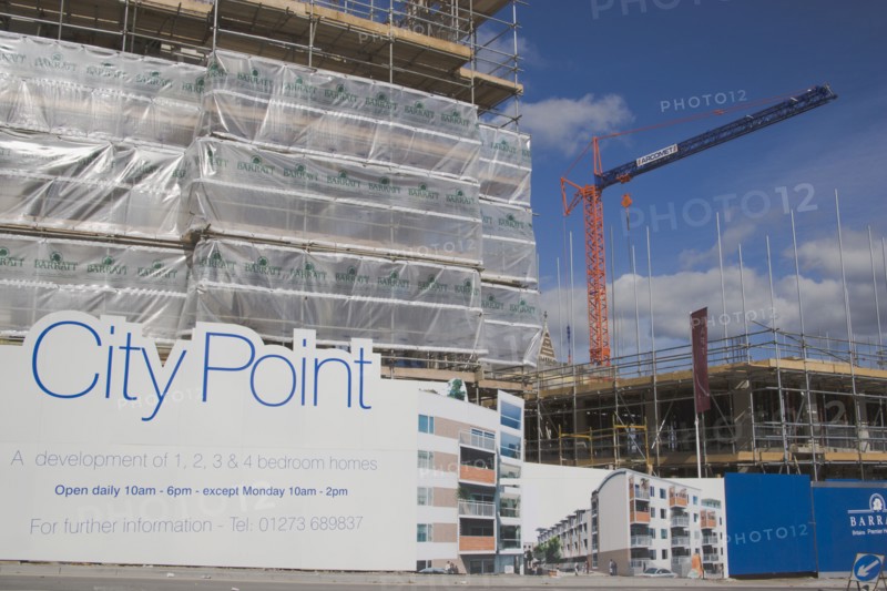 ENGLAND, East Sussex, Brighton, Housing construction site with advertising billboard on view next to road and a large crane in the background.