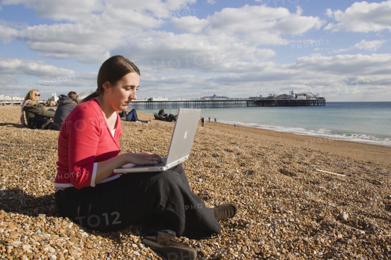 ENGLAND, East Sussex, Brighton, Woman using a laptop to surf the internet  in the free WiFi zone on the beach between the piers
