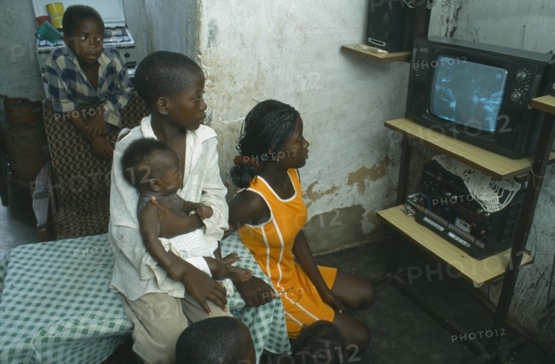 ANGOLA, Luanda, Bairro of Cacuoca.  Fifteen year old Maria Lydia at home watching television with her siblings.  Her family are unable to afford school fees.