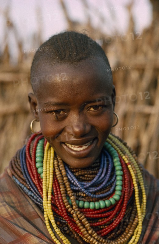 UGANDA, Karamoja District, Portrait of Karamojong woman wearing multiple coloured bead necklaces.  Her hair style indicates her clan.