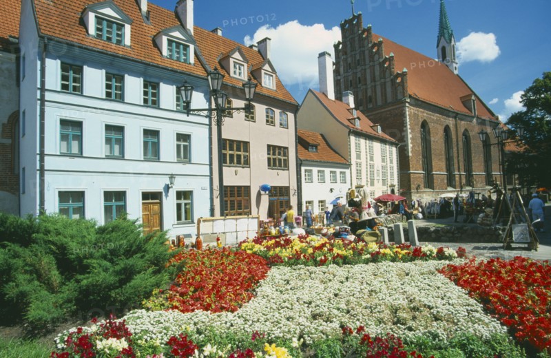 LATVIA, Riga, Church of St John beside town housing with colourful flowerbeds in the foreground on Skunu Street.