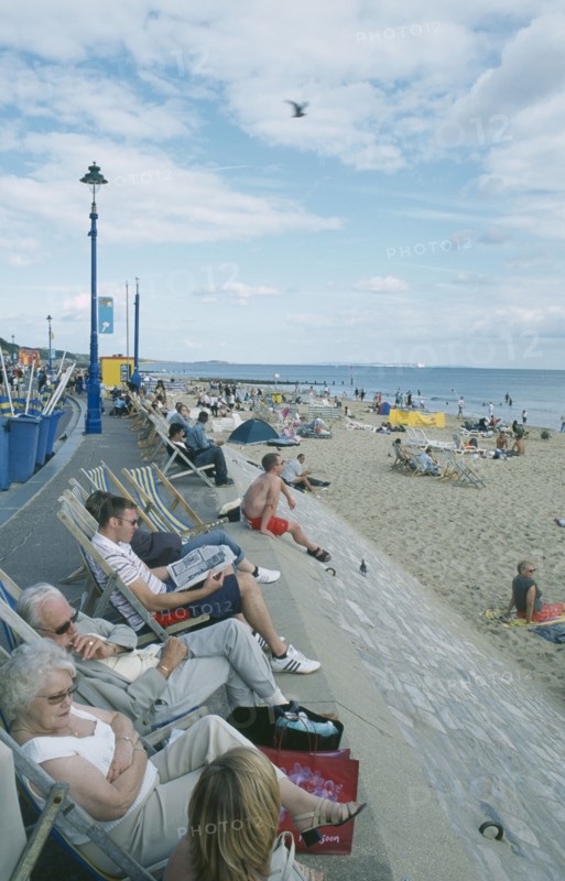 ENGLAND, Dorset, Bournemouth, People sat on deckchairs along seafront.
