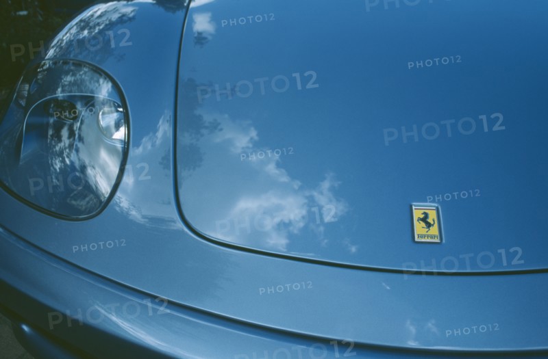 TRANSPORT, Road, Cars, Detail of blue Ferrari emblem and front light with clouds reflected in paintwork.