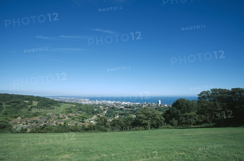ENGLAND, East Sussex, Eastbourne, Elevated view from the South Downs over fields towards town and coastline.