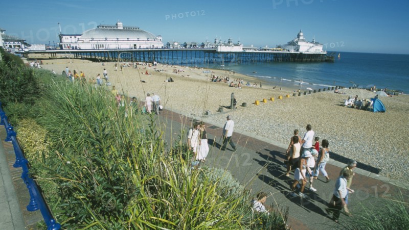 ENGLAND, East Sussex, Eastbourne, View from promenade towards shingle beach and pier with people walking on path.