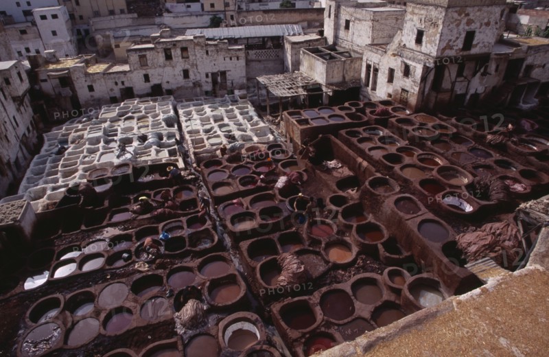 MOROCCO, Fes, Chouwara Tanneries.  Elevated view over the tanner’s pits with city buildings beyond.
