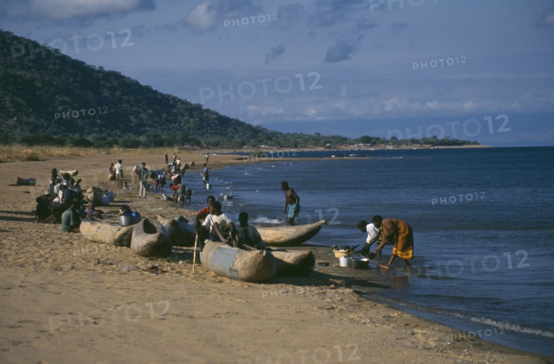 MALAWI, Lake Malawi, Cape Maclear with children playing on shore in wooden canoes and women washing dishes.