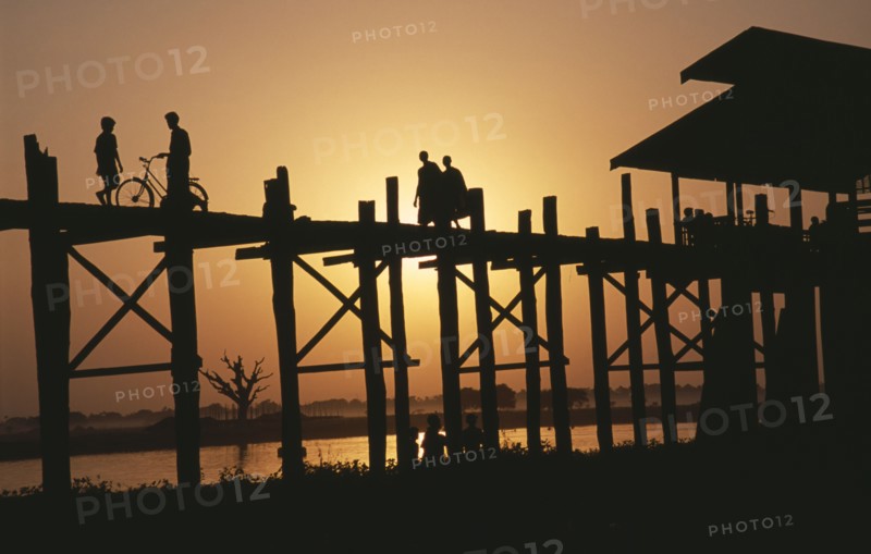 MYANMAR, Amarapura, "U Bein Bridge near Mandalay at sunset with silhouetted figures of monks, child and cyclist crossing."