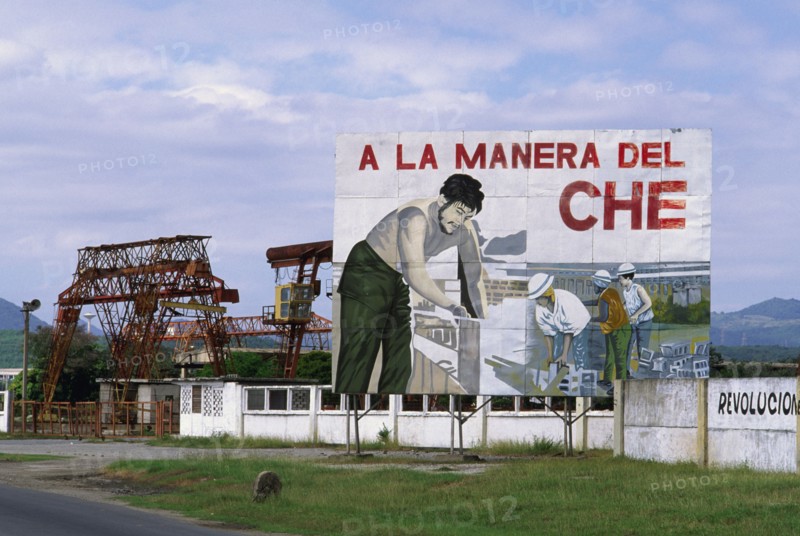 CUBA, Santiago de Cuba, "Billboard celebrating the work of Che Guevara, with industrial facilities behind."