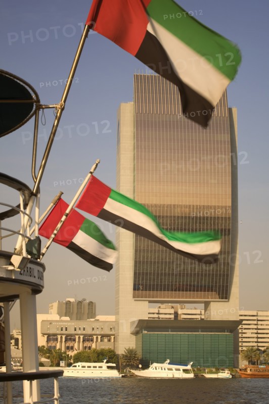 UAE, Dubai, The National Bank with Emirates national flags flying from the stern of a boat in the foreground.