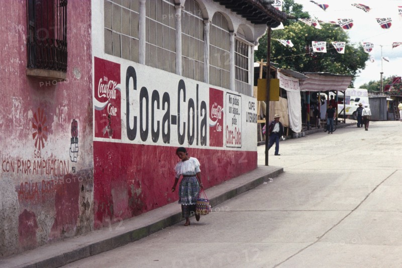 GUATEMALA, Solola, Indigenous woman walks down street past a Coca Cola street sign.