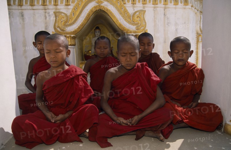 MYANMAR, Amarapura, Young novice monks meditating in front of shrine near Mandalay.