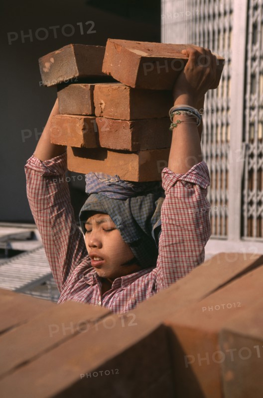 MYANMAR, Mandalay, Female construction worker carrying bricks on her head.