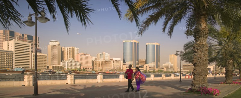 UAE, Dubai, View of Deira across Dubai Creek from Bur Dubai. A couple holding hands and palm trees in the foreground.