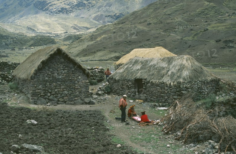 PERU, Cusco, Cancha Cancha, Local Quechuan people weaving in front of dwelling.