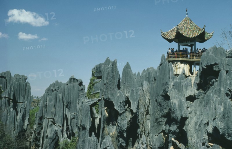 CHINA, Yunnan Province, Shilin, The Stone Forest. Grey limestone rock pinnacles with tourists viewing from under a small traditional roof.