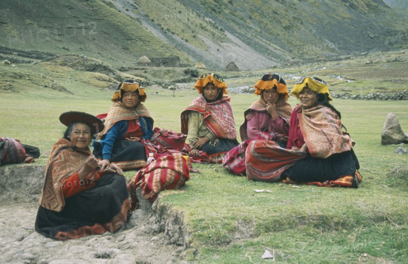 PERU, Cusco, Cancha Cancha, "Local Quechuan women sat on grass, wearing traditional dress."