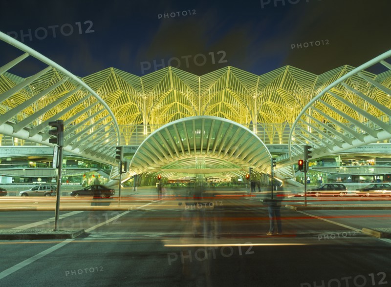 PORTUGAL, Lisbon, Exterior of bus station on the Expo site illuminated at night with light trails from passing traffic and people in blurred movement in foreground.