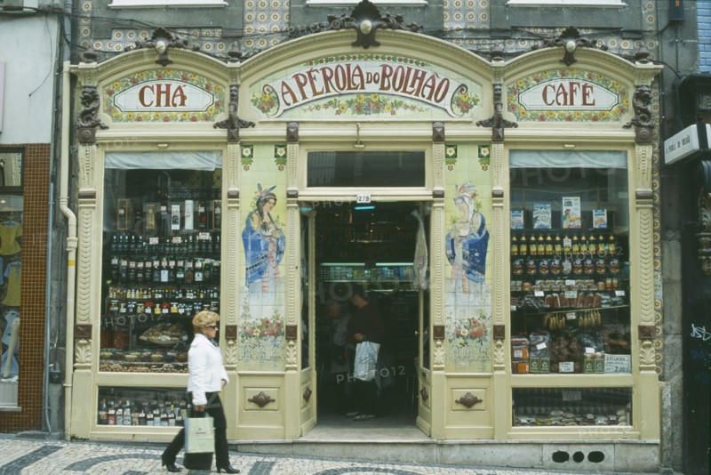 PORTUGAL, Porto, Oporto, "Shop front with mosaic tiling at each side of the doorway and display of dried meat, port and other food items in the windows.  Customers inside and woman walking past."