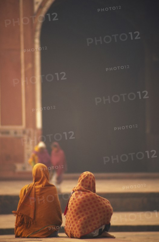 INDIA, Uttar Pradesh, Agra, Two woman sat talking in front of one of the red sand stone buildings that frame the Taj Mahal.