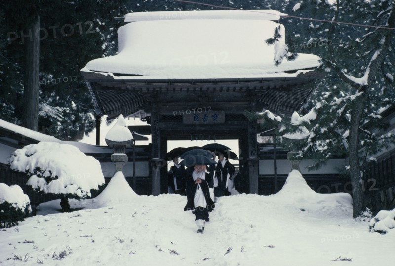JAPAN, Honshu, Kii Peninsula, Mount Koya-san.  Venerated Shingon-Buddhist site.  Novice monks walking through gateway of temple complex in heavy snow.
