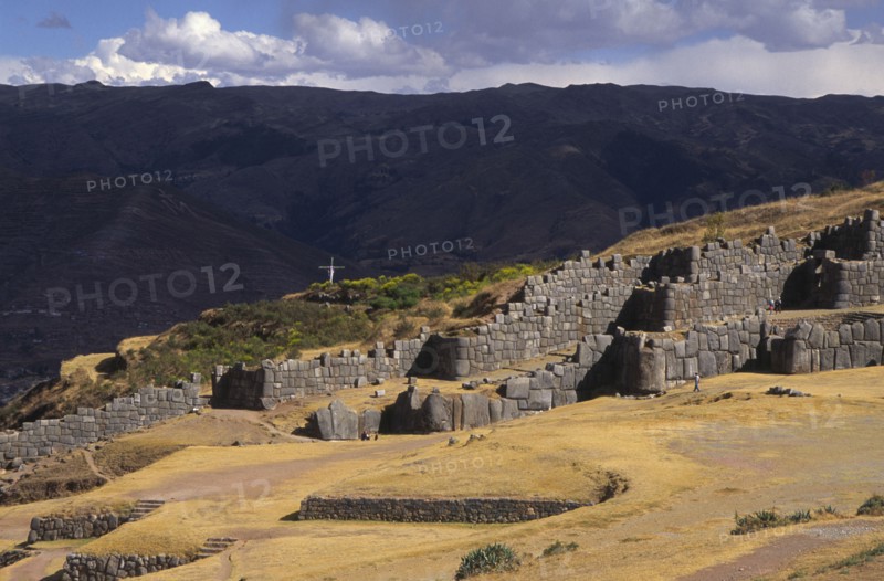 PERU, Cuzco, "Sacsayhuaman inca site, people walking round the old walls and a cross in the background."