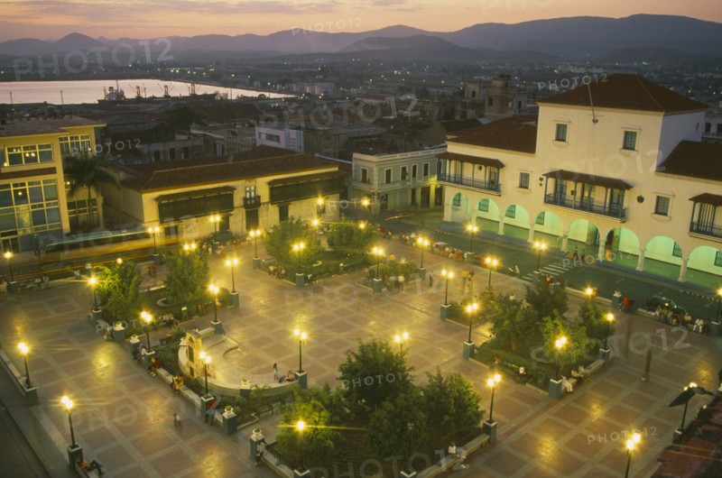 CUBA, Santiago de Cuba, Parque Cespedes at night.  Elevated view over paved square and surrounding buildings with people and street lights.