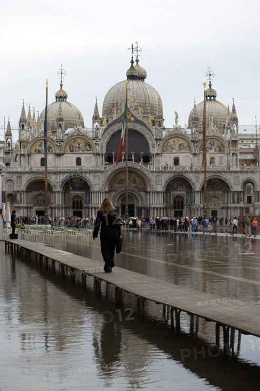 ITALY, Veneto, Venice, Aqua Alta High Water flooding in St Marks Square showing St Marks Basilica at the end of the flooded piazza and a resident walking to work on an elevated walkway