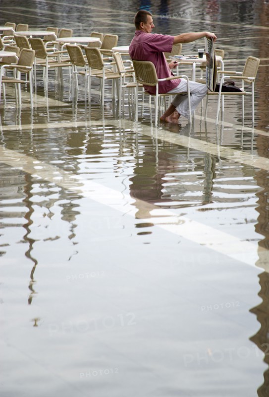 ITALY, Veneto, Venice, Aqua Alta High Water flooding in St Marks Square with an artist painting a watercolour seated at a table in the water of the flooded piazza Paul Seheult