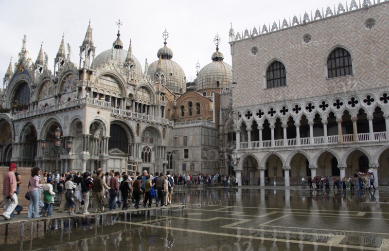 ITALY, Veneto, Venice, Aqua Alta High Water flooding in St Marks Square with tourists walking on elevated walkways above the water beside St Marks Basilica and the Doges Palac