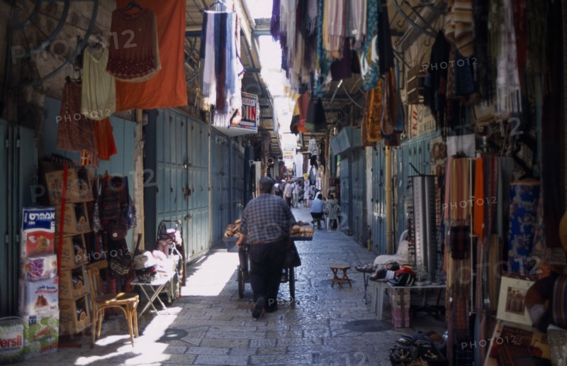 ISRAEL, Jerusalem, An Arab man pushing his bread cart through a narrow street between clothes and textile stalls in the Old City
