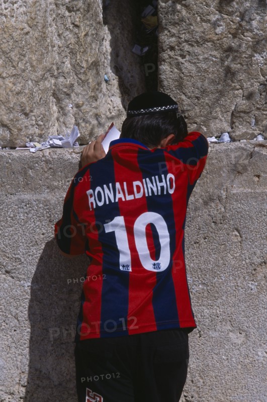 ISRAEL, Jerusalem, An Israeli boy wearing a Ronaldinho football shirt praying at the Western Wall.