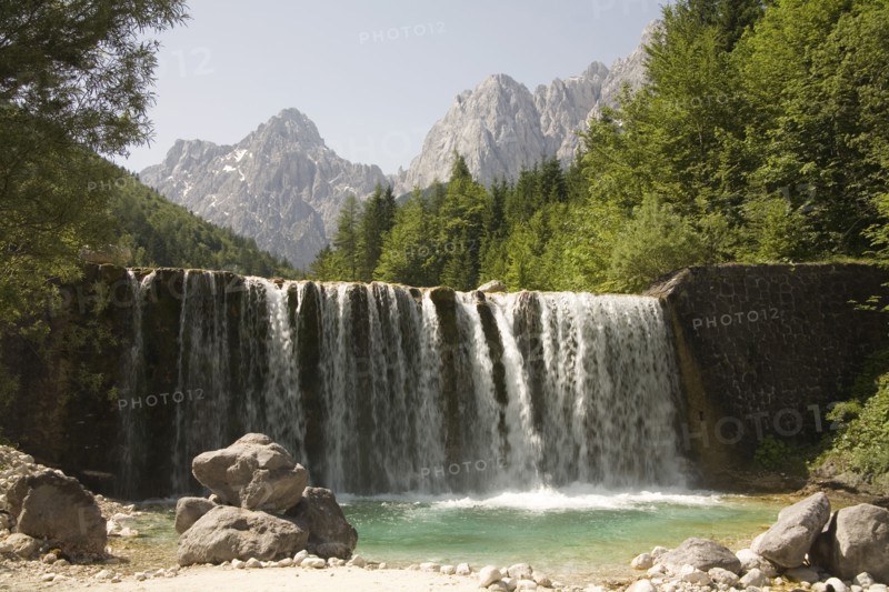 SLOVENIA , Kranjska Gora, Julian Alps, A waterfall on Velika Pisnica with Mounts Razor and Prisank in the Julian Alps in the background. There is still snow lying on the mountain after a severe winter