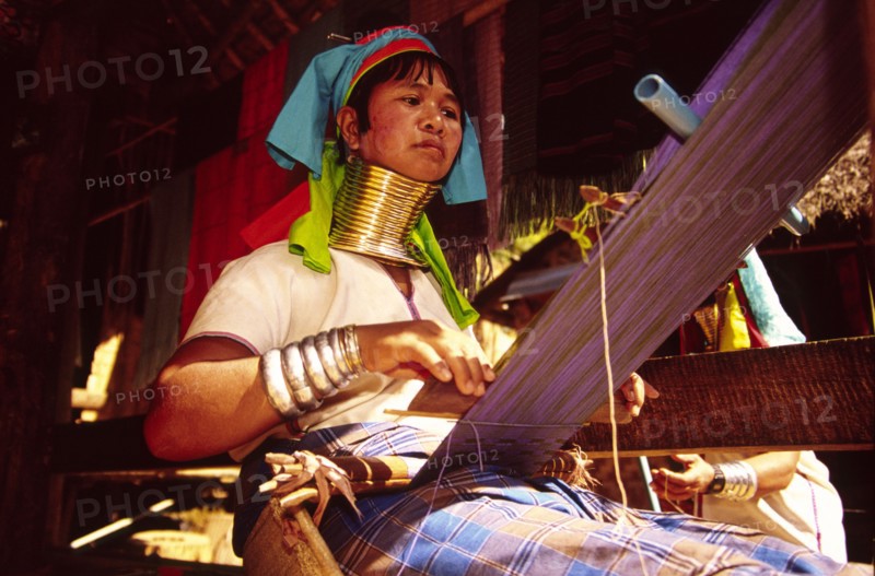 THAILAND, North, Mae Hong Son, "Nai Soi Long neck Karen woman weaving. Nai Soi near the Thai border with Myanmar, is one of several villages where refugee Karen tribals have set up home and use tourism to sustain them. Their necks and legs are traditionally hidden behind an increasing succession of bronze rings which the women must wear from an early age"