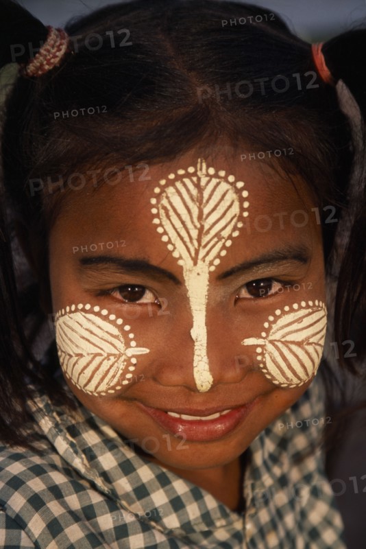 MYANMAR, Amarapura, Head and shoulders portrait of young girl at U Bein Bridge near Mandalay wearing thanakha paste patterns on her face to beautify and protect skin from the sun.