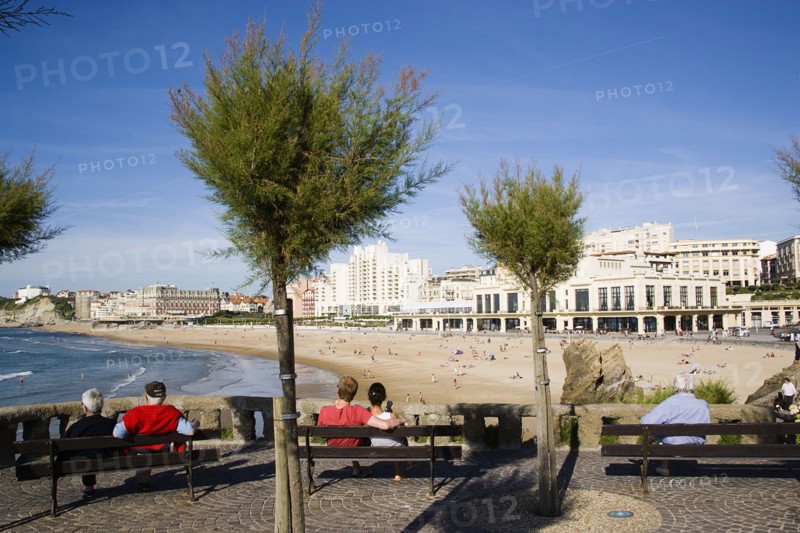 FRANCE, Aquitaine Pyrenees Atlantique, Biarritz, The Basque seaside resort on the Atlantic coast. Tourists sitting on benches beneath tamarisk trees overlooking the Grande Plage beach with the Casino Municipal on the right.