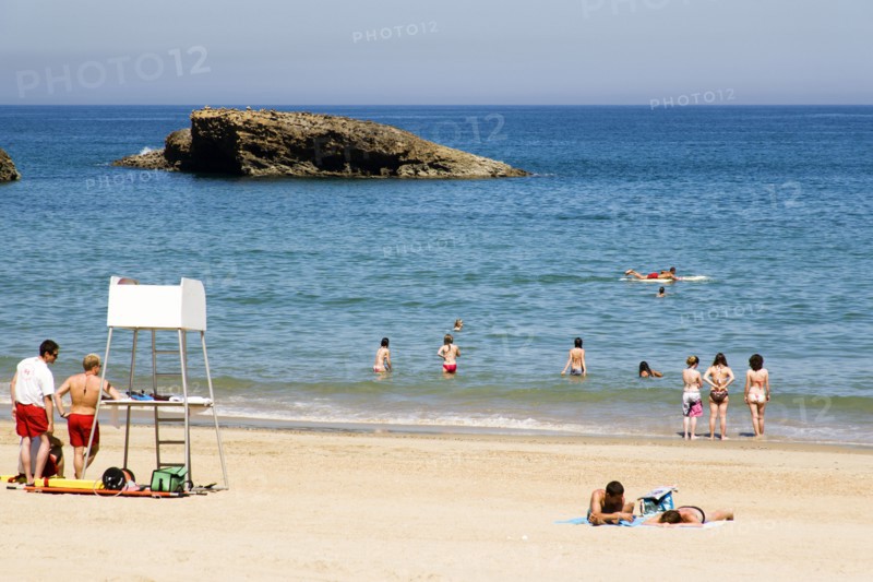 FRANCE, Aquitaine Pyrenees Atlantique, Biarritz, The Basque seaside resort on the Atlantic coast. Lifeguards and young tourists on the Grande Plage beach with a man paddling on a surfboard off the beach